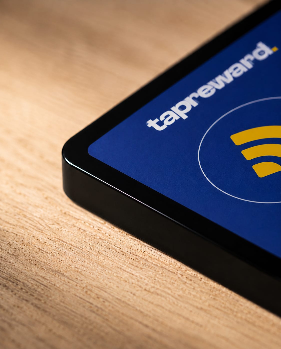 Close detail of the TapReward tap tag on an oak counter, its blue face and yellow tap mark catching the light